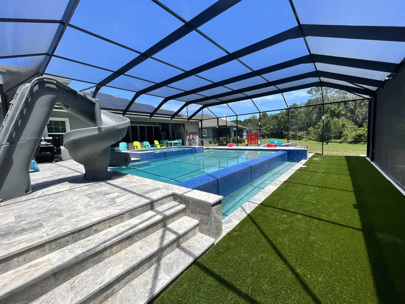 Finished Liquid Lux Pools project in Apollo Beach, 2018: a pool under a screen enclosure with a raised blue mosaic-tile wall, stone steps and a spiral slide