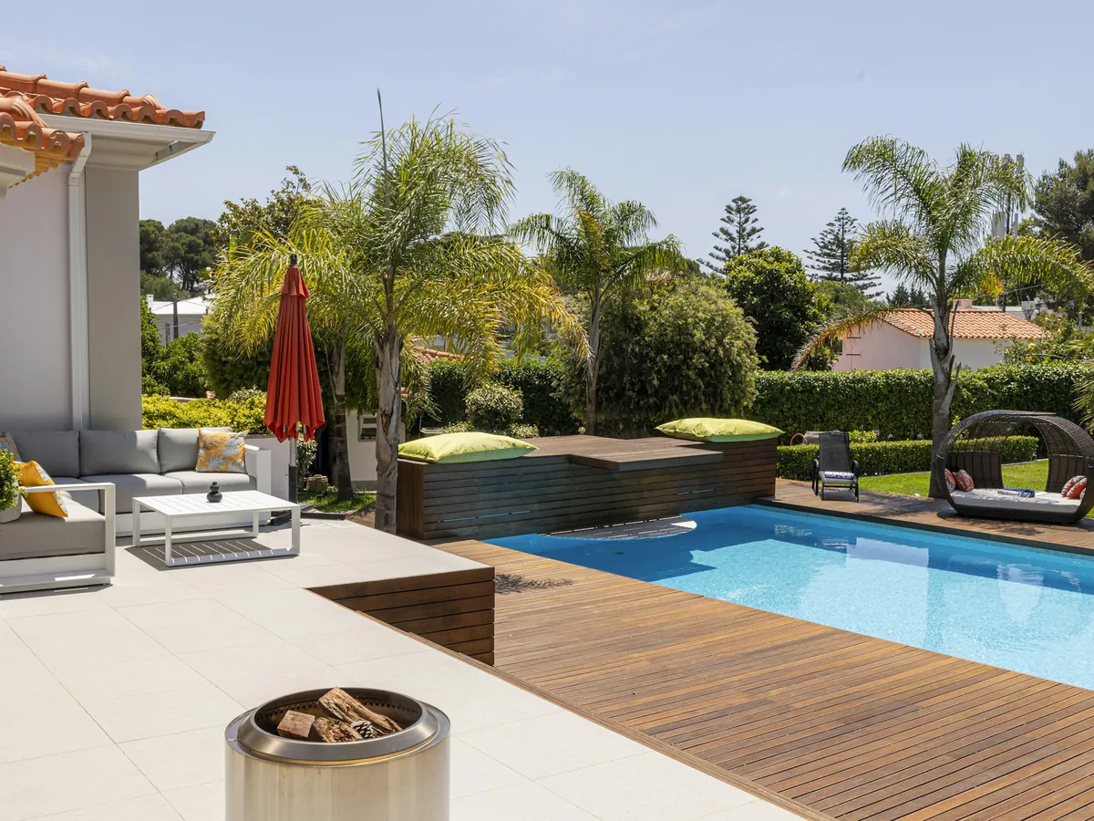 A backyard pool with a teak deck, lounge seating and palms on a sunny day