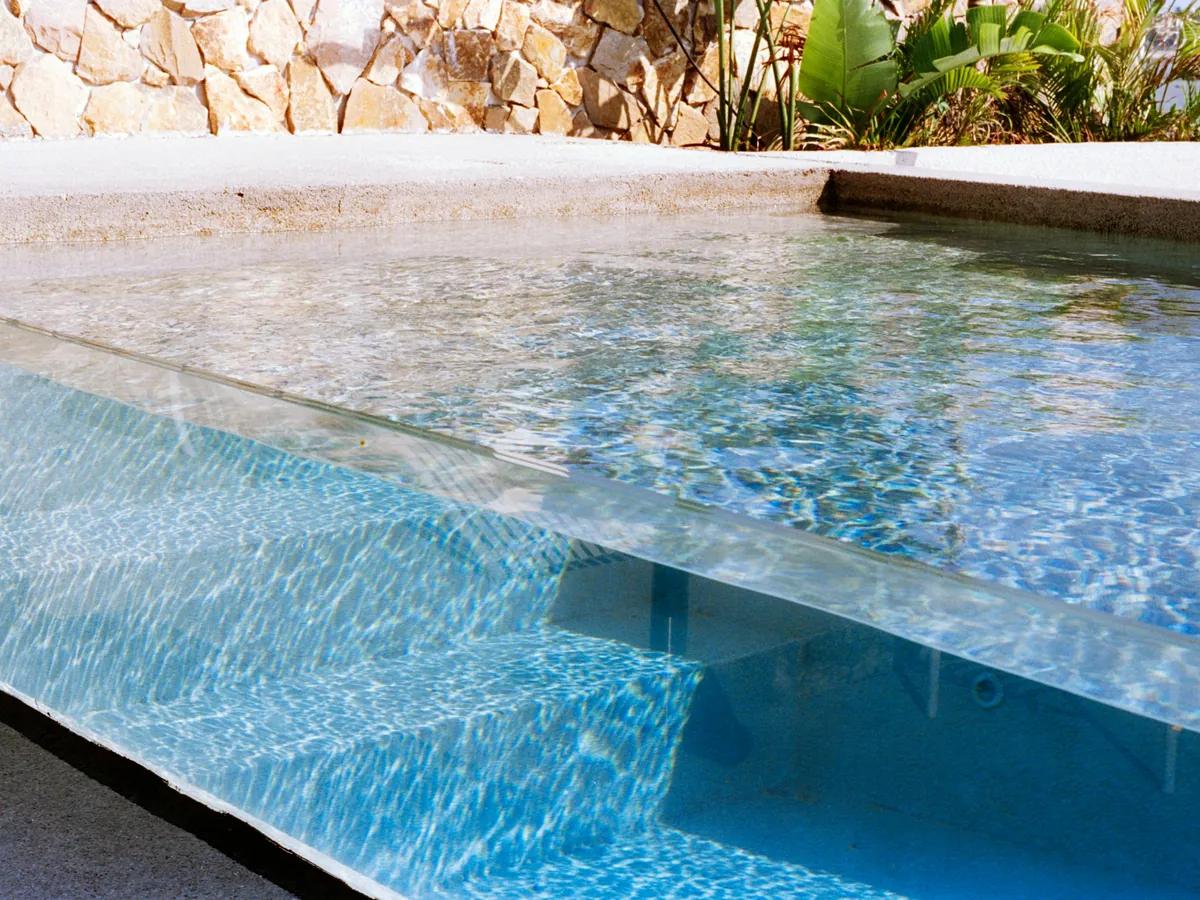 Crystal-clear pool water through a glass-edged wall beside natural stone