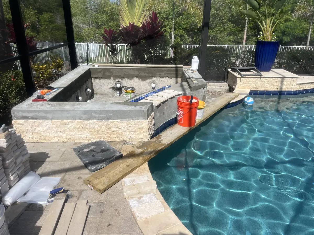 A raised spa under construction beside a pool, its walls clad in stacked stone